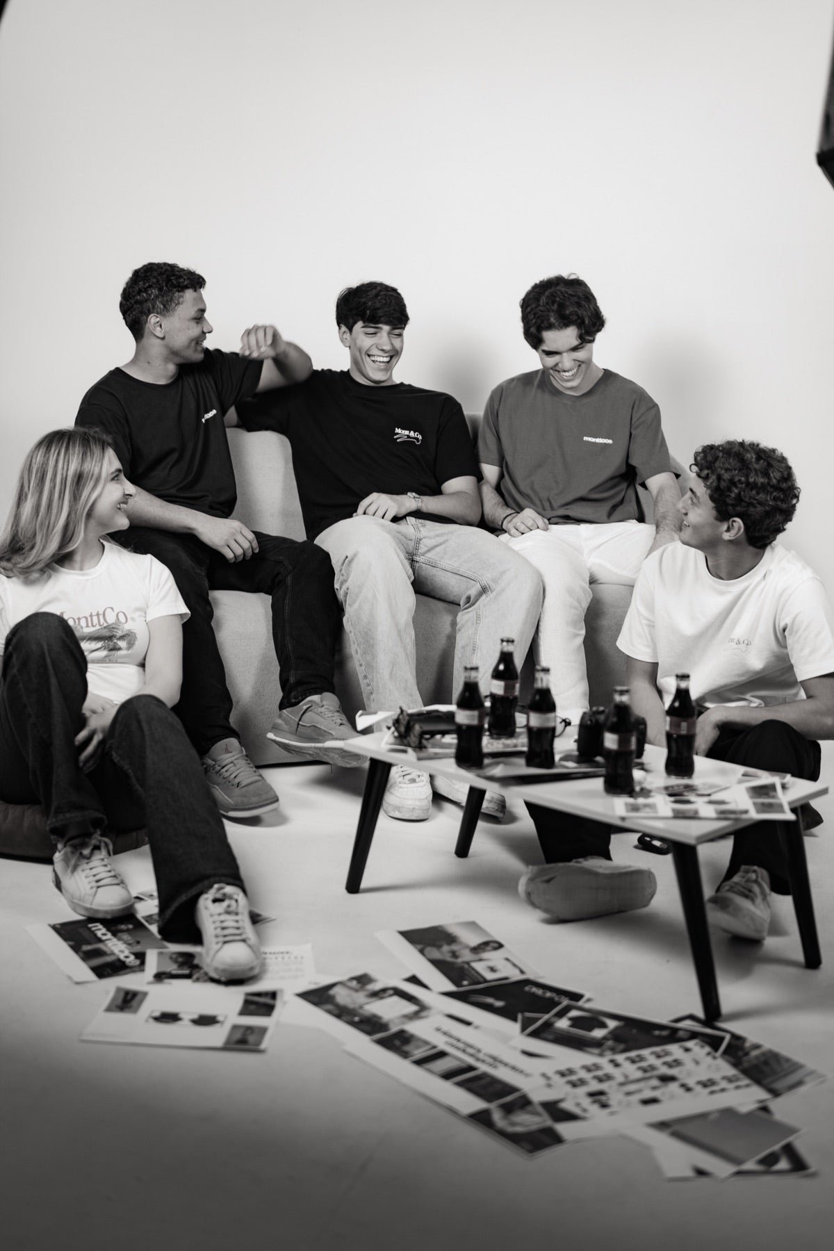 Grupo de amigos sentados, em preto e branco, com adesivos espalhados pelo chão